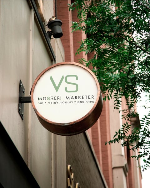 Round storefront sign for VS Mosseri Marketer hanging on a building facade with ivy vines