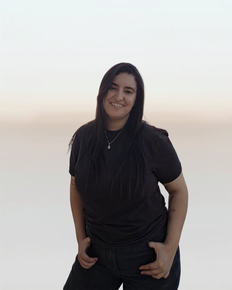 Young woman with long dark hair wearing a black t-shirt, smiling at the camera against a neutral background