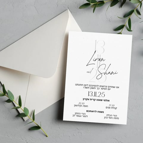 Wedding invitation card for Liren and Shane dated 13.11.25 with Hebrew text, cream envelope, and green sprigs on gray surface