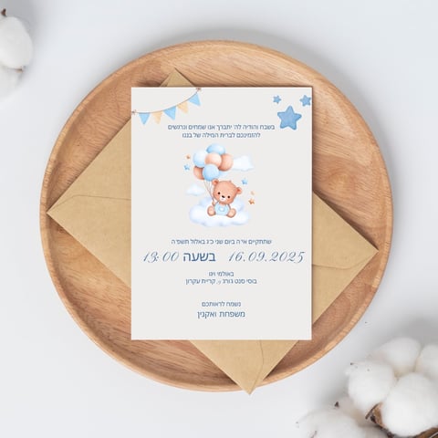 Baby shower invitation card in Hebrew with teddy bear and balloons design, placed on wooden plate with kraft envelopes