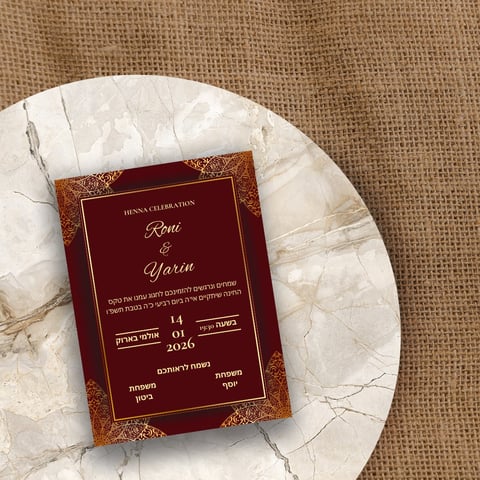 Henna celebration invitation card with red and gold design on white marble plate over burlap background